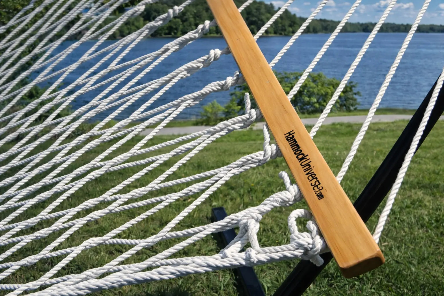 Close-up of a wooden hammock clip attached to a white rope hammock with a lake and trees in the background. 50501-PWT
