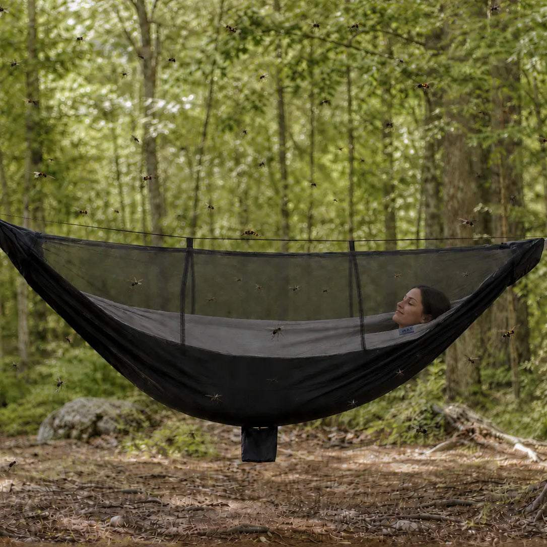 Person in a black hammock with mosquito net in a forest setting