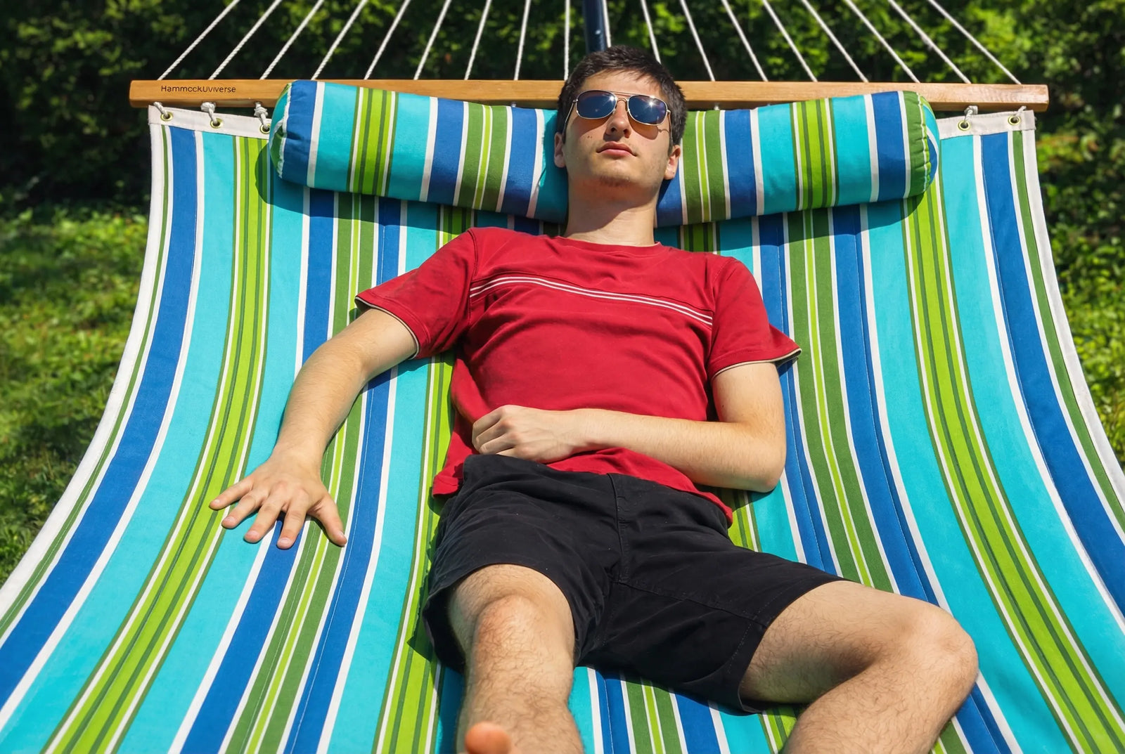 Person relaxing on a colorful striped hammock outdoors QHD-CAROLINA