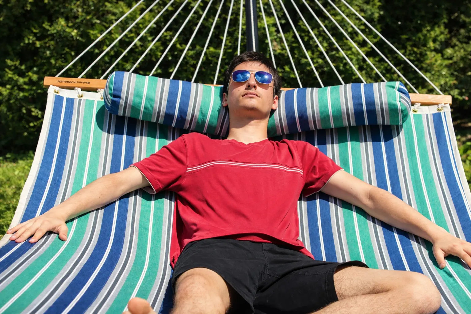 Man relaxing on a striped hammock with armrest pillows in a natural setting QHD-GBGW+15TBSB