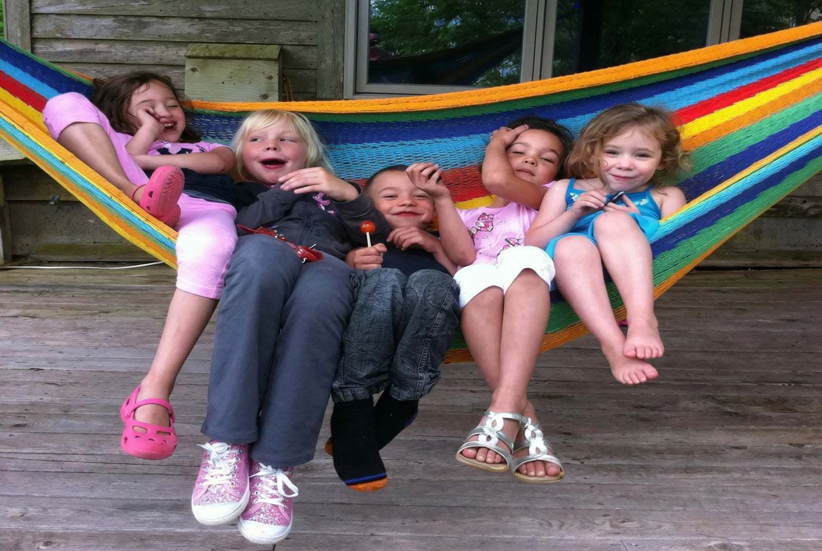 Children sitting on a colorful hammock on a wooden deck #24-MHXLTC-H