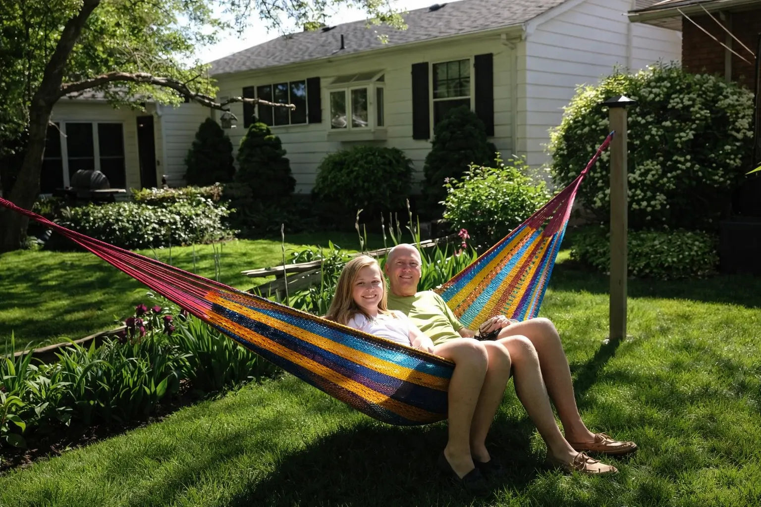 Two people sitting in a colorful hammock in a backyard setting. #24-MHXLTC-H