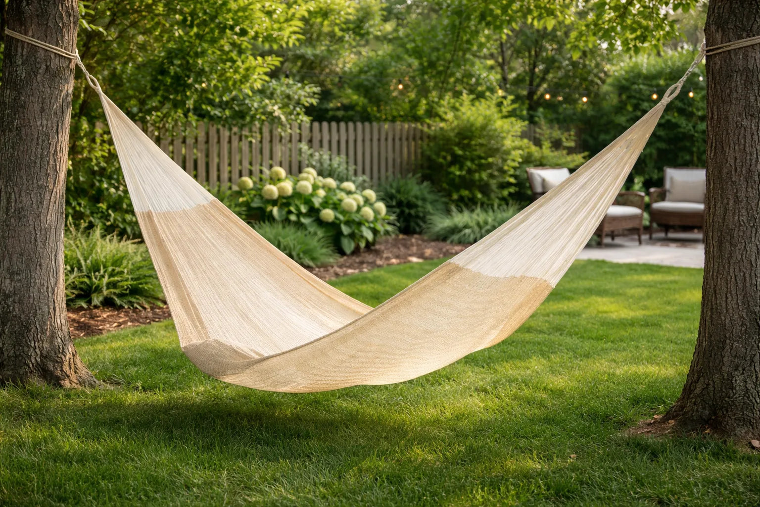 Beige hammock hanging between two trees in a garden setting #24-MHXLTC-N