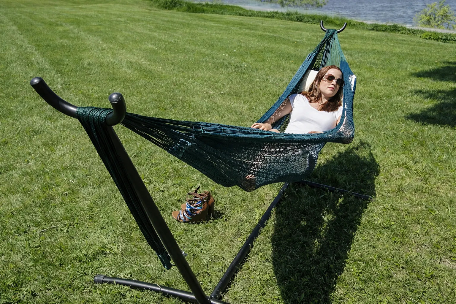 Person relaxing in a green hammock on a grassy field with a stand. #24-MHXLTC-FG+75121