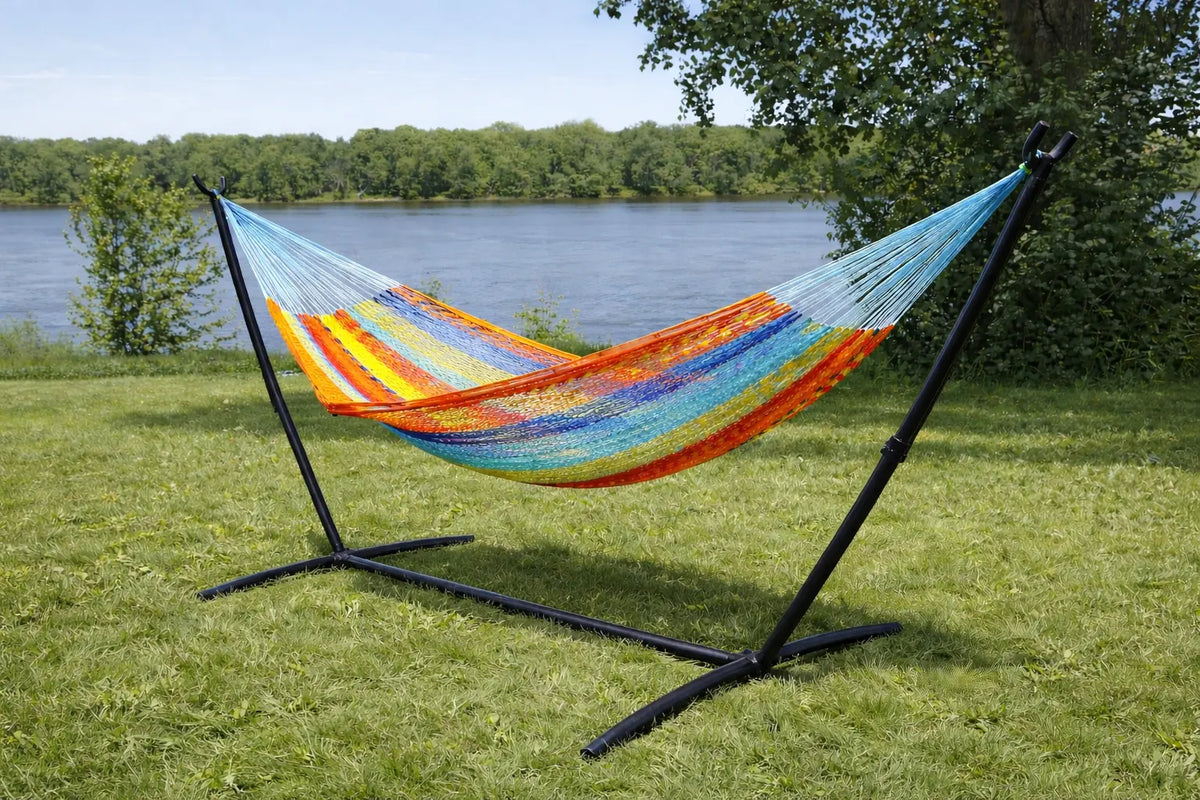 Colorful hammock on a stand in a grassy area near a body of water with trees in the background. #24-MHXLTC-H+75121