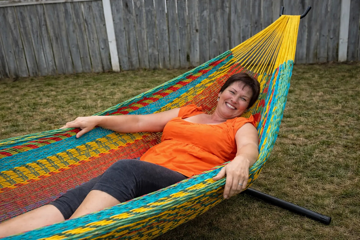 Woman in an orange shirt lying in a colorful hammock outdoors.  #24-MHXLTC-H+75121