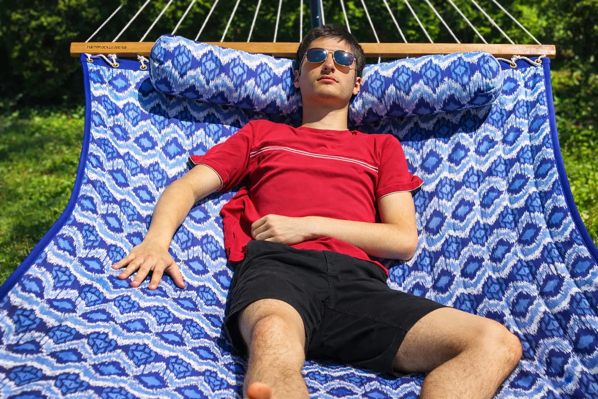 Man lying on a blue patterned hammock outdoors  