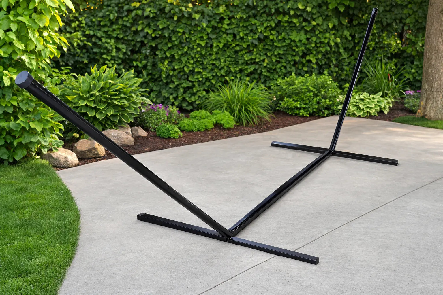 Black metal hammock stand on a concrete patio with greenery in the background  QHD-BWP+15TBSB,QHD-GBGW+15TBSB,QHD-COUNTRY+15TBSB,QHD-CAROLINA+15TBSB