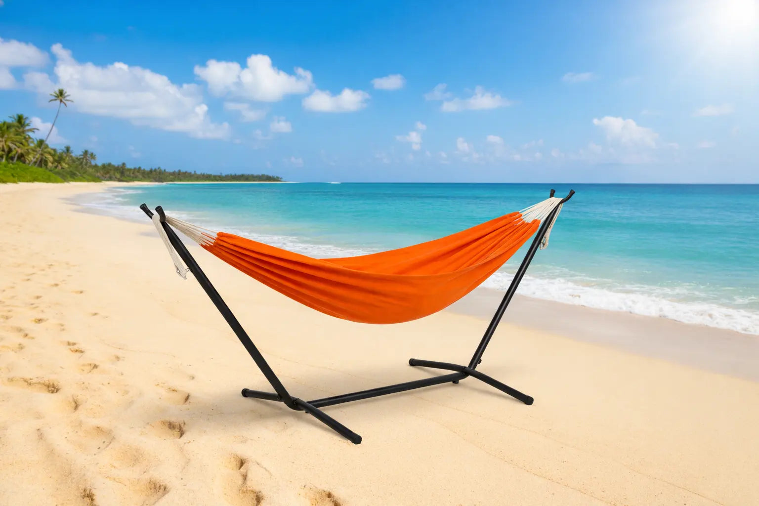 Orange hammock on a black stand on a sandy beach with turquoise water and blue sky.
